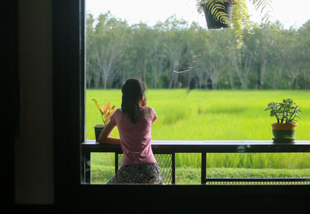 An Asian girl sits on a chair on the balcony, looking at the fields and nature.の写真素材