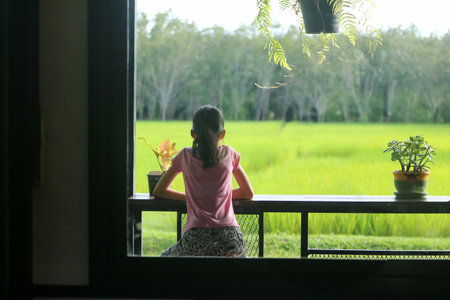 An Asian girl sits on a chair on the balcony, looking at the fields and nature.の写真素材