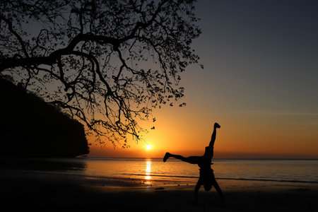 Man playing somersaults on the beach at sunset, red sky in Thailand.の写真素材