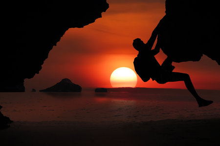Asian man climbing a cliff by the sea As the sun sets around the islands in the Gulf of Thailand, Koh Samuiの写真素材