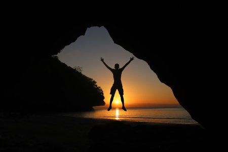 Man jumping on the beach at sunset, beautiful red sky in Thailandの写真素材