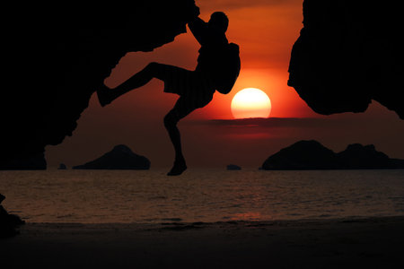 Asian man climbing a cliff by the sea As the sun sets around the islands in the Gulf of Thailand, Koh Samuiの写真素材