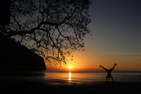 Man playing somersaults on the beach at sunset, red sky in Thailand.の写真素材