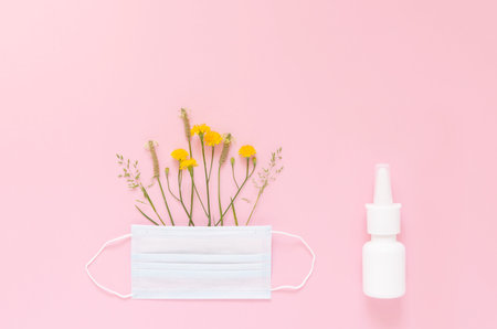 A set of wild flowers and herbs under a disposable protective mask and a mock-up of nasal spray on a light pink background. The concept of means of protection and treatment of seasonal allergiesの写真素材
