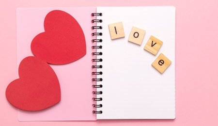 The word Love is laid out in wooden letters on the page of an open notebook, next to it are two red hearts. The concept of a love letter on Valentine's Day, Mother's Day, a declaration of loveの写真素材