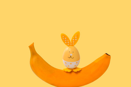 A cheerful Easter bunny is sitting on a ripe banana. yellow festive background