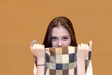 Portrait of a young woman with a disappointed, anxious expression, hugging a pillow