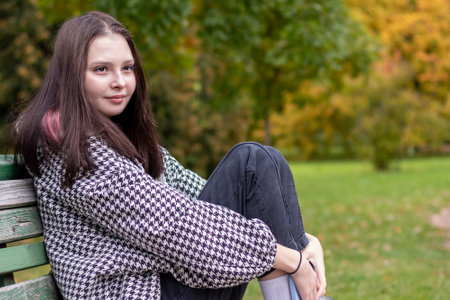Close-up of a young woman sitting on a bench in an autumn parkの写真素材