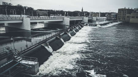 Reservoirs are open with flowing water and bridge above. Cloudy sky in winter.の写真素材