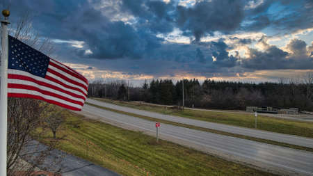 American flag stands against rural road under moody sky.