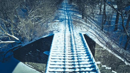 Snowmobile tracks over old bridge in winter on overgrown trail.