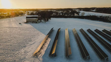 Snow covers the land around a old barn and rows of solar panelsの写真素材