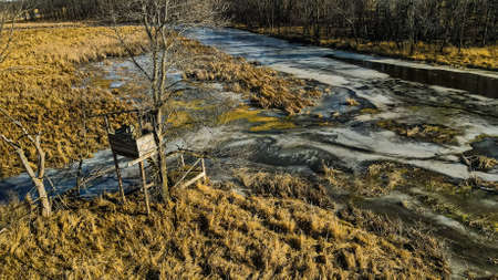 A very old and weathered hunting blind still stands in the meadow with frozen standing water.