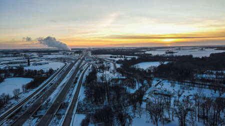 Snow covered land over highway and smoke from power plant in distance.の写真素材