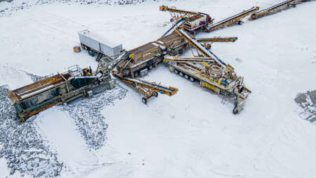 Snow covers the land while heavy machines at the quarry are still in use.の写真素材