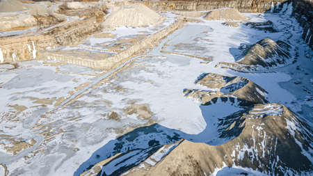 Snow covered rock quarry in winter with massive piles of gravel and stone.
