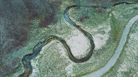 The snow has melted and spring has arrived. A view of a spiraling stream with a trail alongside it in a rural area.の写真素材