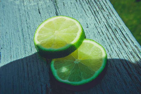 Sitting out on the bright sun a pair of sliced limes on a blue wooden deckの写真素材
