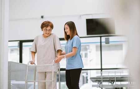 young physical therapist helping senior patient in using walker during rehabilitationの写真素材