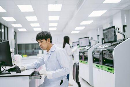 young male scientist looking results from automation blood analyzer report in computer and young female scientist working with automation blood analyzer at medical laboratoryの写真素材