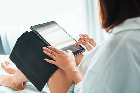 young woman working on tablet computer while sitting at the bedroom. work from home conceptの写真素材