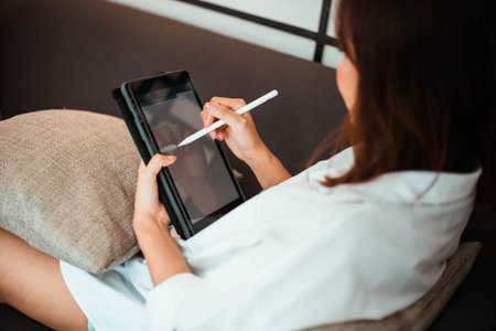 young woman working on tablet computer while sitting at the bedroom. work from home conceptの写真素材