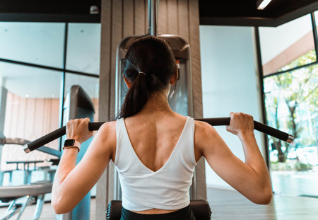 Close up back of young woman in sportswear working out with machine in gymの写真素材