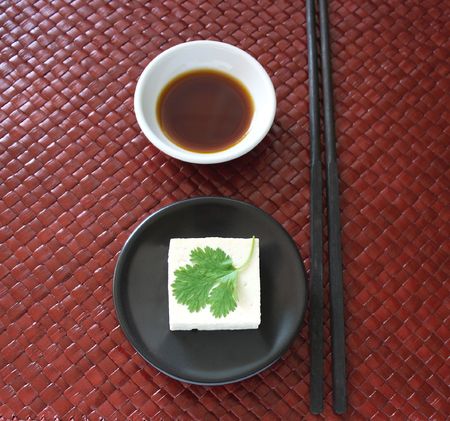 a square of tofu topped with a single cilantro leaf on a round blackの写真素材
