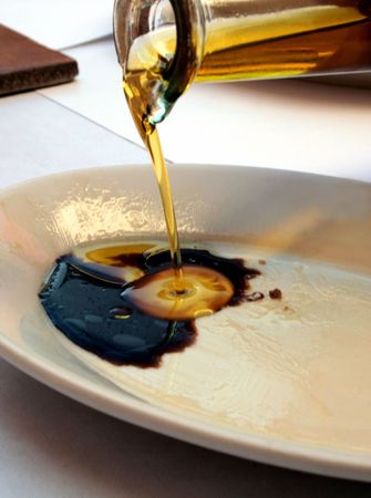 olive oil being poured into balsamic vinegar on a white plateの写真素材