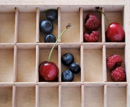 cherries and berries in the compartments of a wood type caseの写真素材