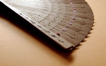 a light brown Chinese hand fan partially unfolded on textured paperの写真素材