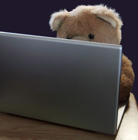 a teddy bear at a laptop against a black backgroundの写真素材