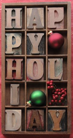 happy holiday in old wood letters in a type case with ornaments and berries