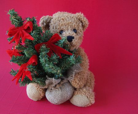 a toy bear holds a Christmas tree decorated with red velvet bows and copy spaceの写真素材