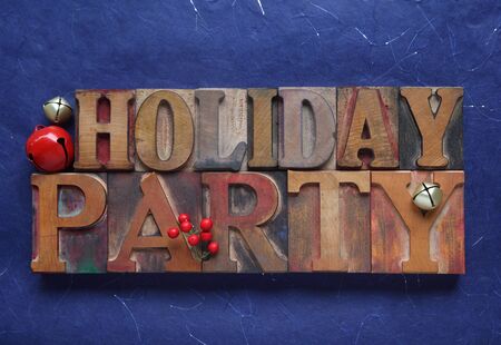 the words holiday party in old wood type with red and gold bells and berriesの写真素材