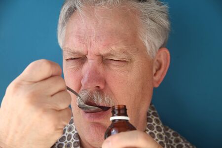 sick man frowns as he takes a spoonful of cough syrupの写真素材