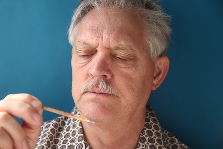 older man frowns as he looks at his temperature