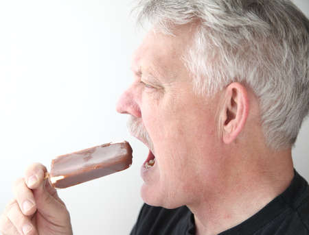 an older man eats a chocolate-covered ice cream barの写真素材
