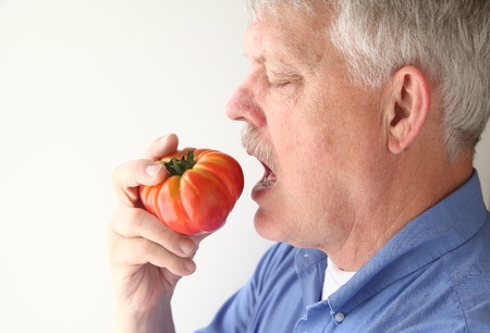 older man ready to bite into an heirloom tomatoの写真素材