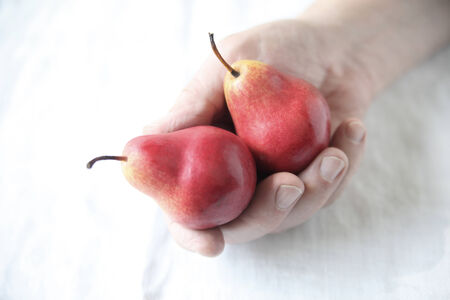 a man holding small red pears against a white tableclothの写真素材