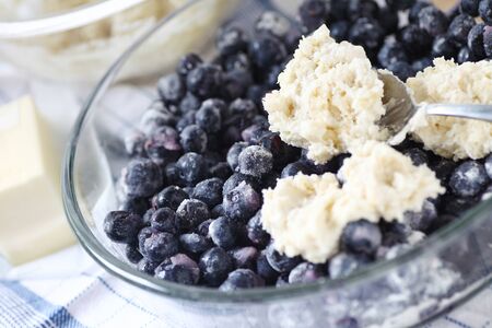 Spooning biscuit dough onto a bowl of sugared blueberriesの写真素材