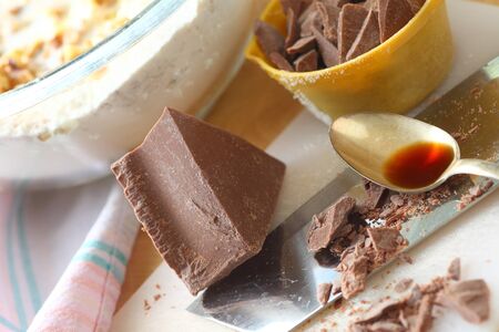 Block of chocolate some chopped in measuring cup with vanilla and mixing bowl of batterの写真素材