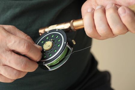 A man holds a fly fishing rod and reel.