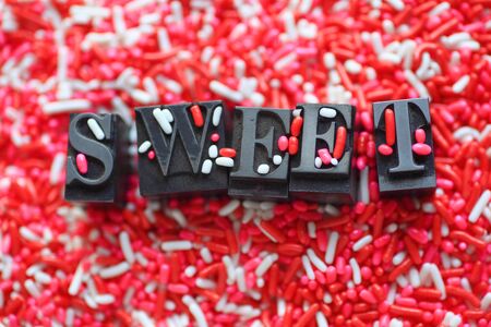 The word 'sweet' in metal type on a pink and white candy sprinkles backgroundの写真素材
