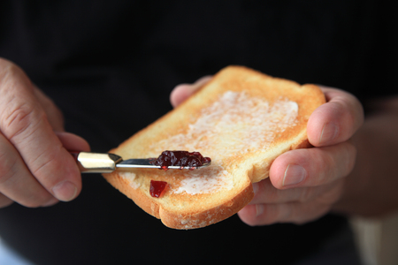 Older man spreads grape jam on a slice of buttered toast, copy space included.