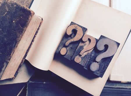 Three letterpress wood type question marks on blank pages of vintage book