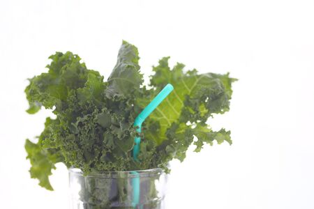 Fresh kale leaves in a drinking glass with a pale blue straw and copy spaceの写真素材