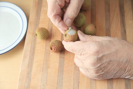 A man begins to peel a fresh lychee on a cutting board.