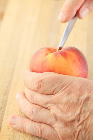 A man cuts into a peach with a paring knife.の写真素材