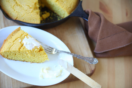 Portion of cornbread with butter with the rest in a cast iron skillet behind